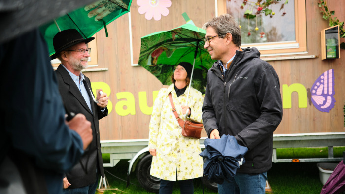 Staatssektretär Dr. Andre Baumann steht mit Regenschirm vor dem Natourbauwagen im Rahmen der KLIMA.LÄND.TAGE 2024.