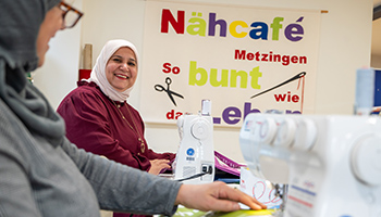 Bei einer Aktion der Klimaländetage sitzen im Nähcafè Metzingen zwei Frauen an Nähmaschinen. Eine Frau strahlt Richtung Kamera.