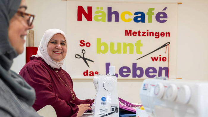Bei einer Aktion im Rahmen der KLIMA.LÄND.TAGE 2024 sitzen im Nähcafè Metzingen zwei Frauen an Nähmaschinen. Eine Frau strahlt Richtung Kamera.