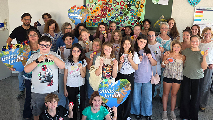 Kinder der Schulklasse der Hebelschule Bretten halten gehäkelte Blumen und Schilder der Omas for Future in den Händen und lächeln zur Kamera.