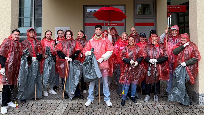 Gruppenfoto der Mitarbeitenden der Kreissparkasse Freudenstadt in roten, durchsichtigen Regencapes und rotem Regenschirm