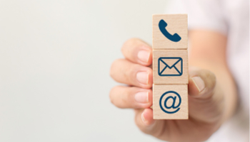 Eine Person hält drei quadratische Würfel mit Symbolen für ein Telefon, einen Briefumschlag und eine E-Mail in der Hand.
