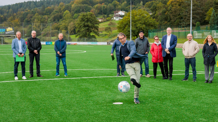 Staatssekretär Dr. Andre Baumann spielt einen Fußball über den Sportplatz.